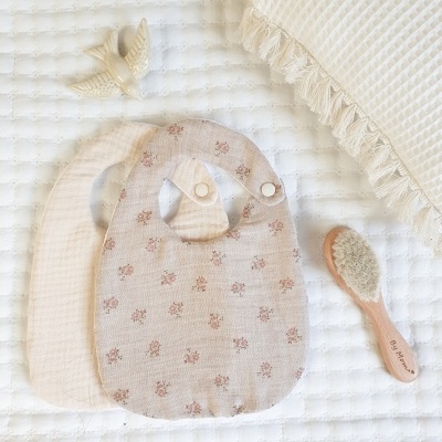 Dois babetes para bebé em tecido macio, uma escova de cabelo em madeira e tecido branco acolchoado