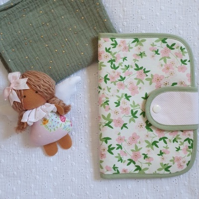 Fralda verde, boneca de pano e carteira floral em fundo branco texturizado
