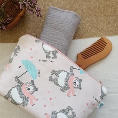 Necessaire rosa claro com padrão de ursos e guarda-chuvas, com toalha cinzenta e pente castanho à vista