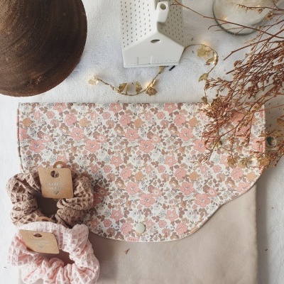 Bolsa bege com aba floral e scrunchies em tecido junto a casa decorativa em cerâmica e flores secas.