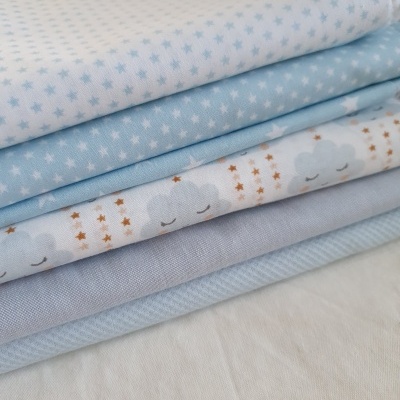Tecidos dobrados em tons azuis e branco com padrões de estrelas e nuvens