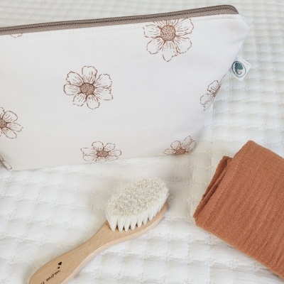 Necessaire branca com flores castanhas, escova de cabelo de madeira e tecido castanho claro sobre superfície branca