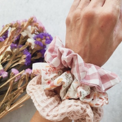 Três scrunchies coloridos no pulso com flores secas ao lado