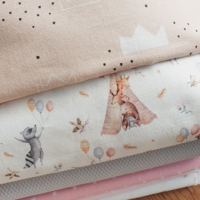 Conjunto de têxteis infantis com vários padrões e cores, empilhados sobre madeira