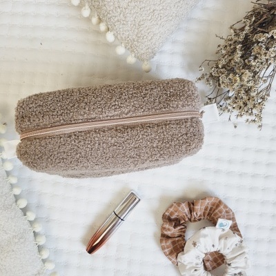 Estojo castanho felpudo, baton metálico e elásticos para cabelo estampados sobre tecido branco