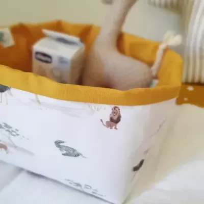 Cesto tecido branco com borda amarela e animais estampados, com brinquedo e caixa no interior