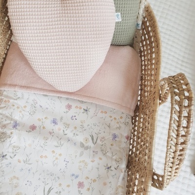 Berço de vime com almofadas rosa e verde e edredão floral