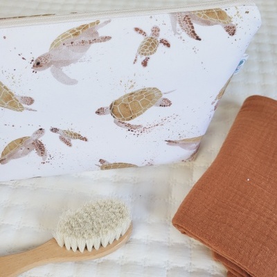 Necessaire com padrão de tartarugas, escova de madeira e tecido laranja sobre fundo branco acolchoado