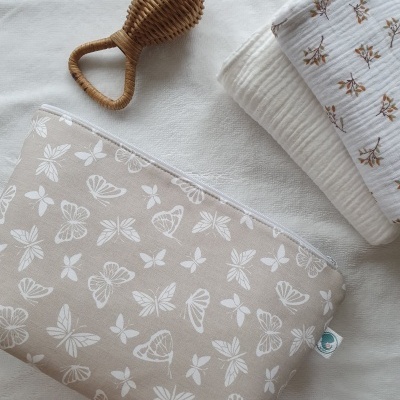 Estojo bege com borboletas brancas, escova de rattan e tecidos dobrados em fundo claro