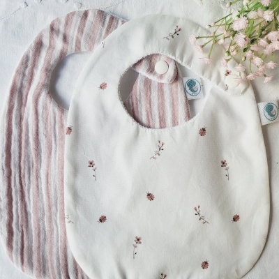 Dois babetes de bebé em tecido, um branco com flores e outro com riscas cor-de-rosa e branco
