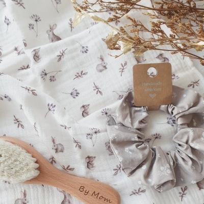 Escova de madeira com cerdas brancas e elástico de tecido cinzento sobre pano branco com padrão de coelhinhos