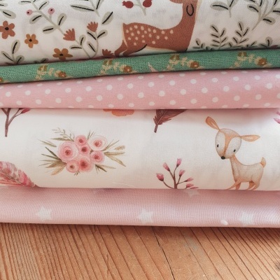 Tecidos dobrados com padrões de veados, flores, folhas e bolinhas em rosa, branco, verde e bege.