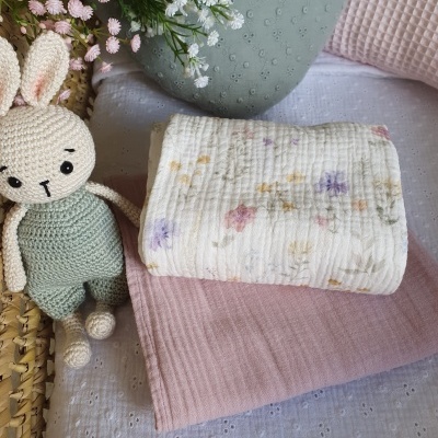 Boneco de coelho de crochê junto a tecidos rosa e branco floral sobre superfície branca texturizada