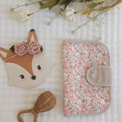 Carteira floral rosa e bege, máscara de raposa com flores e brinquedo de madeira sobre tecido branco