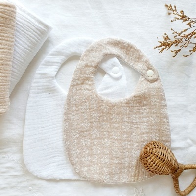 Dois babetes para bebés, branco e bege, com botão de pressão.