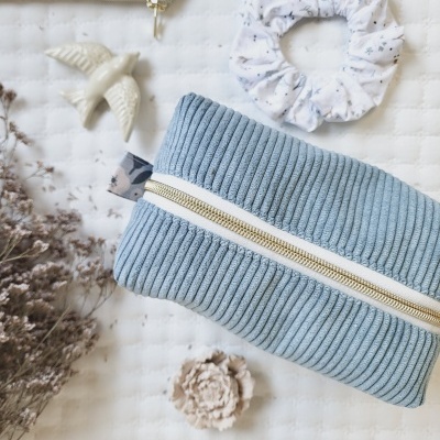 Estojo azul com fecho dourado e prendedor de cabelo em fundo branco matelassado