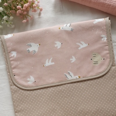 Estojo rosa com estampa de pássaros brancos e padrão de pontos brancos sobre fundo bege