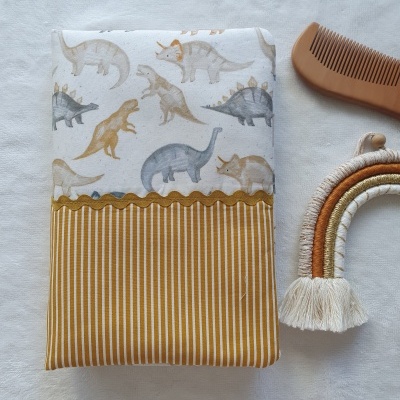 Produto de tecido com padrão de dinossauros e riscas, pente de madeira e arco decorativo em tons terrosos