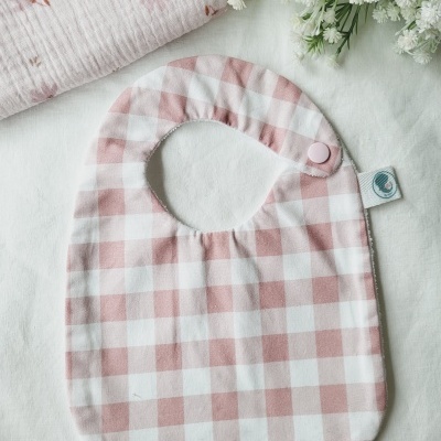 Babete de bebé xadrez rosa e branco com botão e flores ao lado