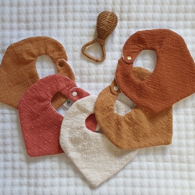 Babetes de tecido em tons terra com fecho de pressão e mordedor castanho sobre fundo branco acolchoado