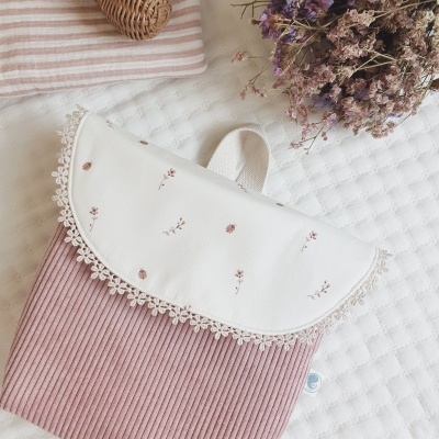 Bolsa pequena de tecido rosa com tampa branca bordada e renda, sobre tecido branco matelassado com flores secas ao lado