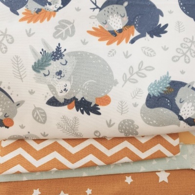 Tecidos empilhados com padrões de ursos, chevron e estrelas em cores neutras e laranja.