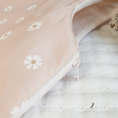 Capa rosa claro estampada com flores brancas e amarelas com zíper, em superfície acolchoada branca.