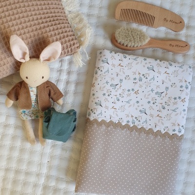 Jogo para bebé com toalha bege, fralda floral, rabano e escova de madeira, brinquedo coelho de tecido e pano bege texturizado.