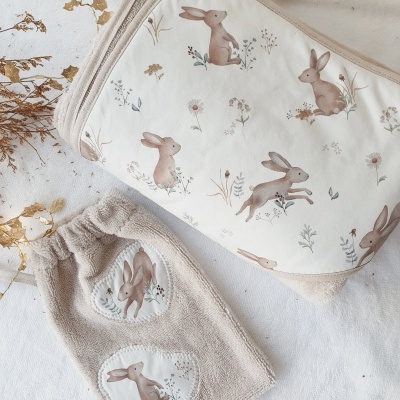 Necessaire e fralda com padrão de coelhos castanhos em fundo branco e bege, com folhas secas ao redor