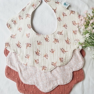 Três babetes para bebé com padrões florais e bordas onduladas sobre fundo branco com flores.