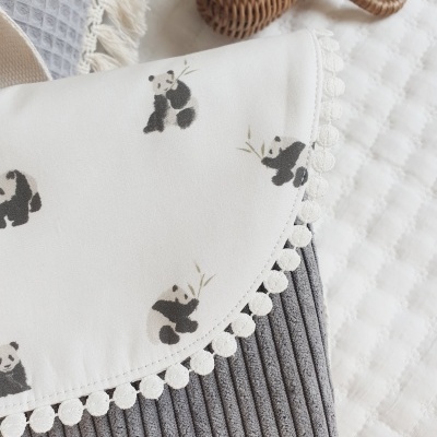 Capa cinzenta com aba branca decorada com pandas e pompons, com tecido acolchoado e objeto de rattan
