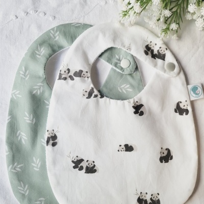 Dois babetes de bebê, um branco com pandas e outro verde com folhas brancas.