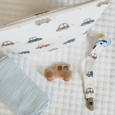 Bolsa branca com padrão de carros, manta azul, brinquedo de madeira de carro e chupeta azul com fita estampada