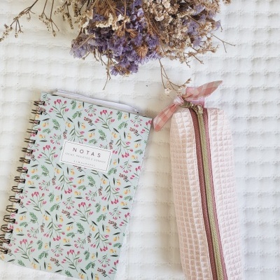Caderno floral, necessaire rosa texturizada e flores secas sobre pano branco texturizado