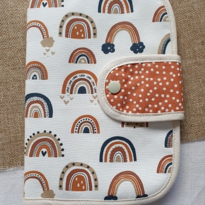 Capa de tecido branca com padrão de arcos-íris e aba alaranjada com bolinhas brancas