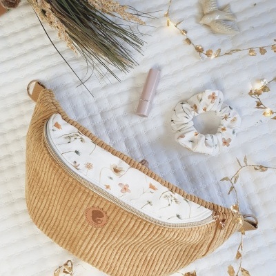 Bolsa bege canelada com bolso floral e acessórios sobre tecido branco acolchoado