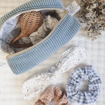 Bolsa azul aberta com chocalho e acessórios de cabelo em fundo branco