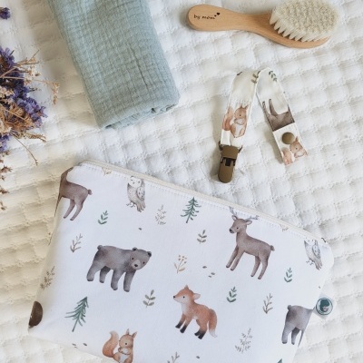 Bolsa estampada com animais da floresta e acessórios de bebé sobre tecido acolchoado branco