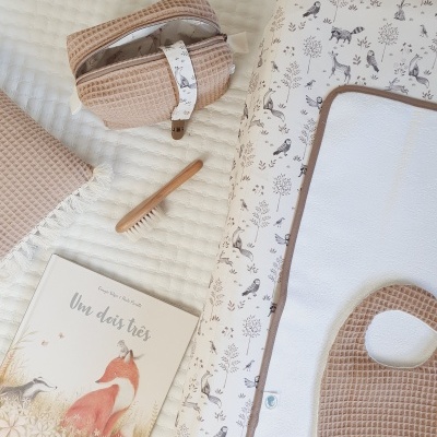 Toalha bege, bolsa com padrão animal, escova de madeira, almofada com estampa animal e livro infantil com raposa