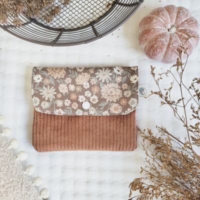 Carteira em veludo cor de ferrugem com aba floral sobre superfície branca com abóbora e ramos secos