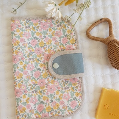 Carteira ou estojo com padrão floral e fecho azul sobre tecido branco com flores secas e sabão amarelo