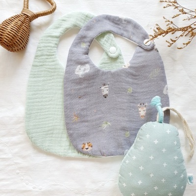 Babetes de tecido macio com estampas e textura, e brinquedo em forma de pêra, em superfície branca.