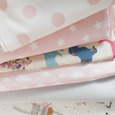Diferentes tecidos empilhados com padrões de bolinhas, estrelas, coelhos e nuvens em tons de rosa e branco.
