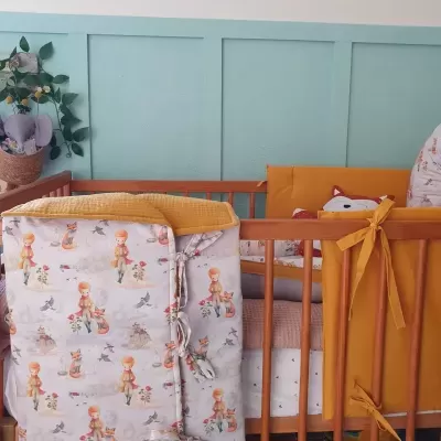 Berço de madeira com roupa de cama amarela e branca com padrão de personagens, almofada decorativa, parede verde-azulada