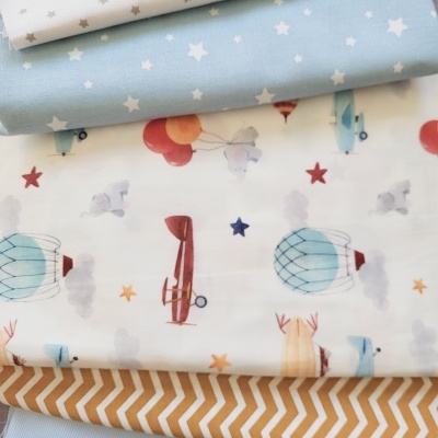 Tecidos com padrões de estrelas, balões, aviões e zig-zag em várias cores dobrados sobre uma superfície.