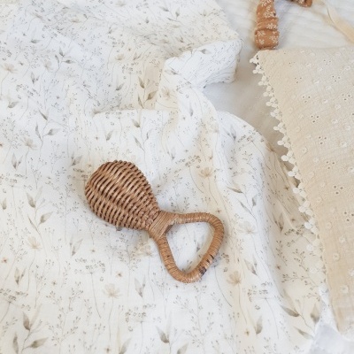 Manta branca com padrão floral, chupeta de rattan e almofada bege com renda