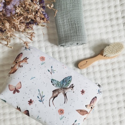 Saco de pano com desenhos de animais, escova de cabelo de madeira, tecido verde e flores secas sobre superfície branca