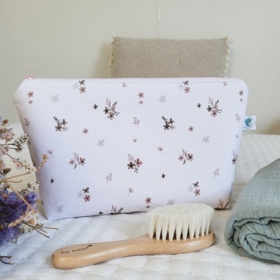 Necessaire branca com flores, escova de cabelo de madeira e toalha verde num ambiente de quarto