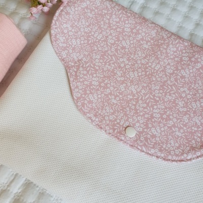 Bolsa de tecido branca com aba rosa claro floral e botão de pressão em superfície branca texturada