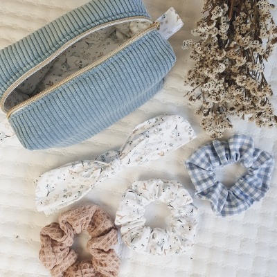 Necessaire azul clara com elásticos para cabelo e flores secas sobre tecido branco